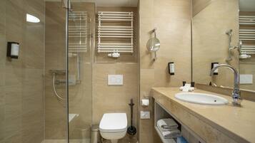 Un baño moderno con cabina de ducha de vidrio, un inodoro blanco, un lavabo con espejo y un perchero para toallas.