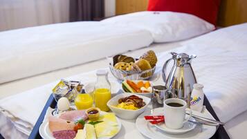 A breakfast tray with eggs, bacon, ham, cheese, and juice on a bed with white bedding and a red pillow.