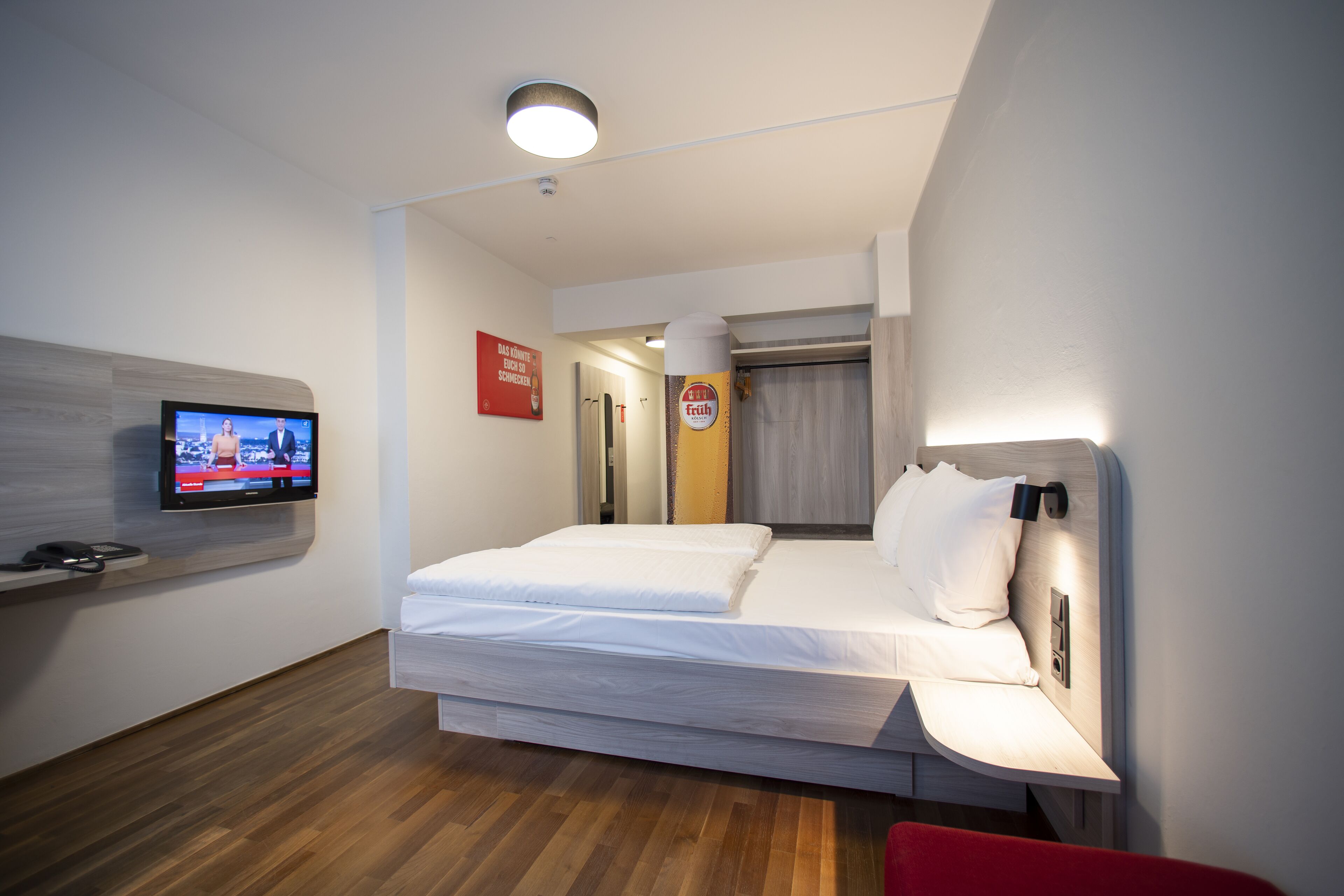 Une chambre d’hôtel moderne équipée d’un lit, d’un téléviseur à écran plat, d’un plancher en bois et d’un fauteuil rouge.