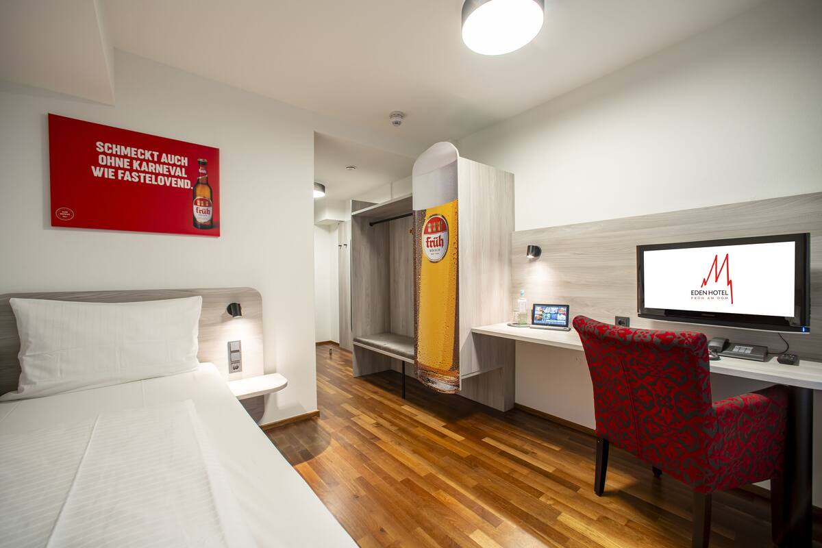 A hotel room with a bed, a desk with a computer, a chair, and a shower area.