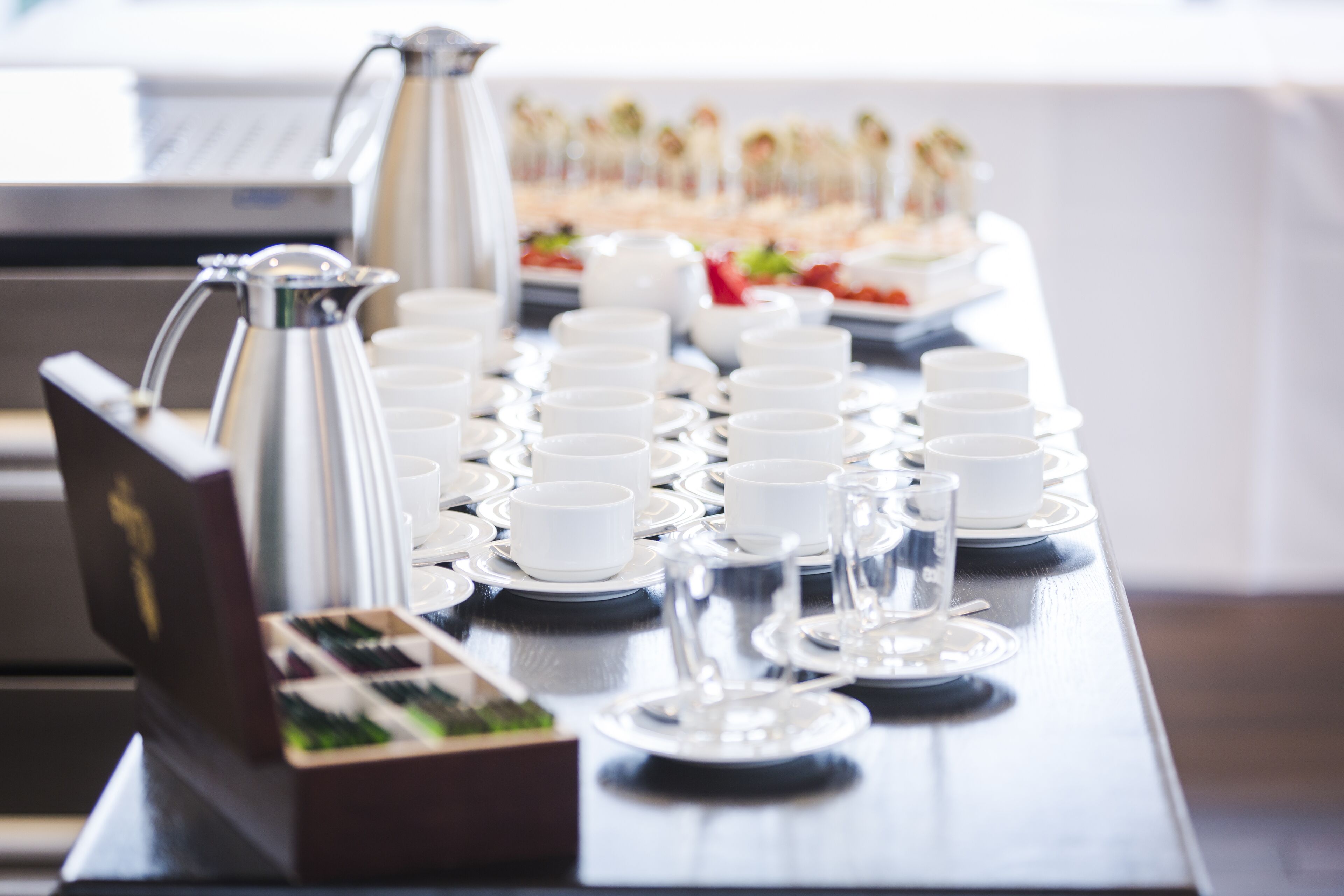Een buffetopstelling met meerdere witte kopjes en schoteltjes, een koffiepot en een schaal met eten.