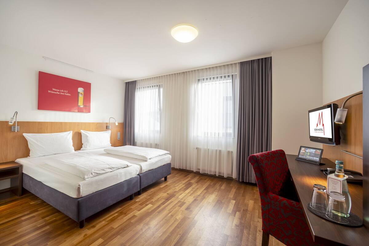 A hotel room with a wooden floor, two beds, a desk with a computer, and a TV.