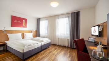 Una habitación de hotel con piso de madera, dos camas, un escritorio con computadora y un televisor.