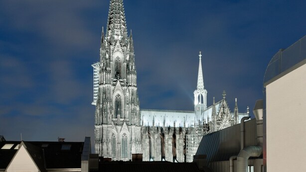 Une terrasse sur le toit, avec une table dressée pour un mariage, deux lanternes et une cathédrale en arrière-plan.