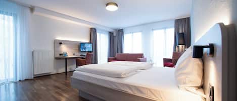 A modern hotel room with a large bed, a desk with a computer, and a TV.