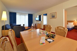 Une chambre d’hôtel avec une table en bois, des chaises, un canapé, une télévision et un lit.