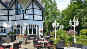An outdoor patio with tables and chairs, surrounded by a building with a white facade and black trim. - Gut Funkenhof (Sundern)