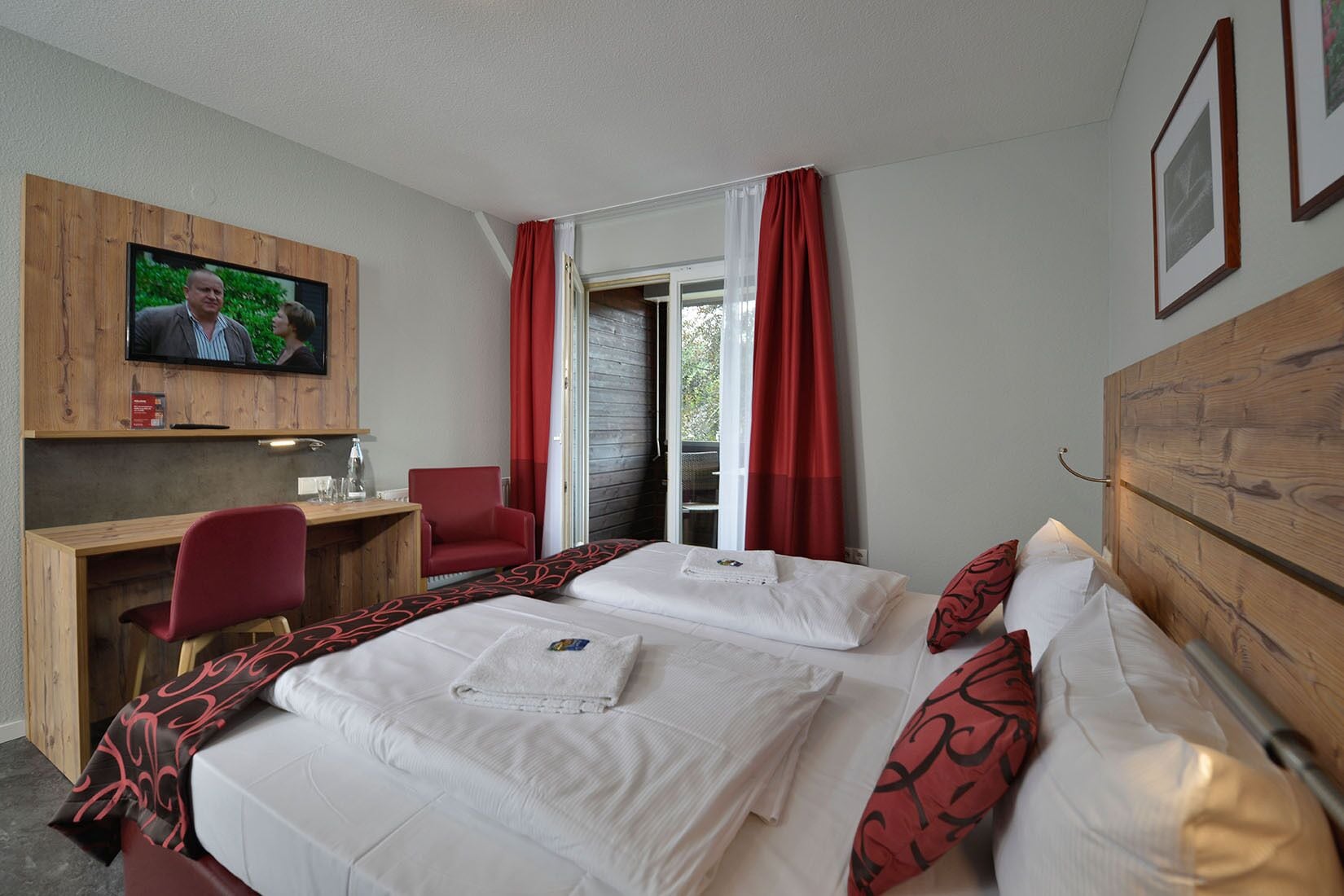Una habitación de hotel con una cama, un escritorio con silla, un televisor y una ventana con cortinas.