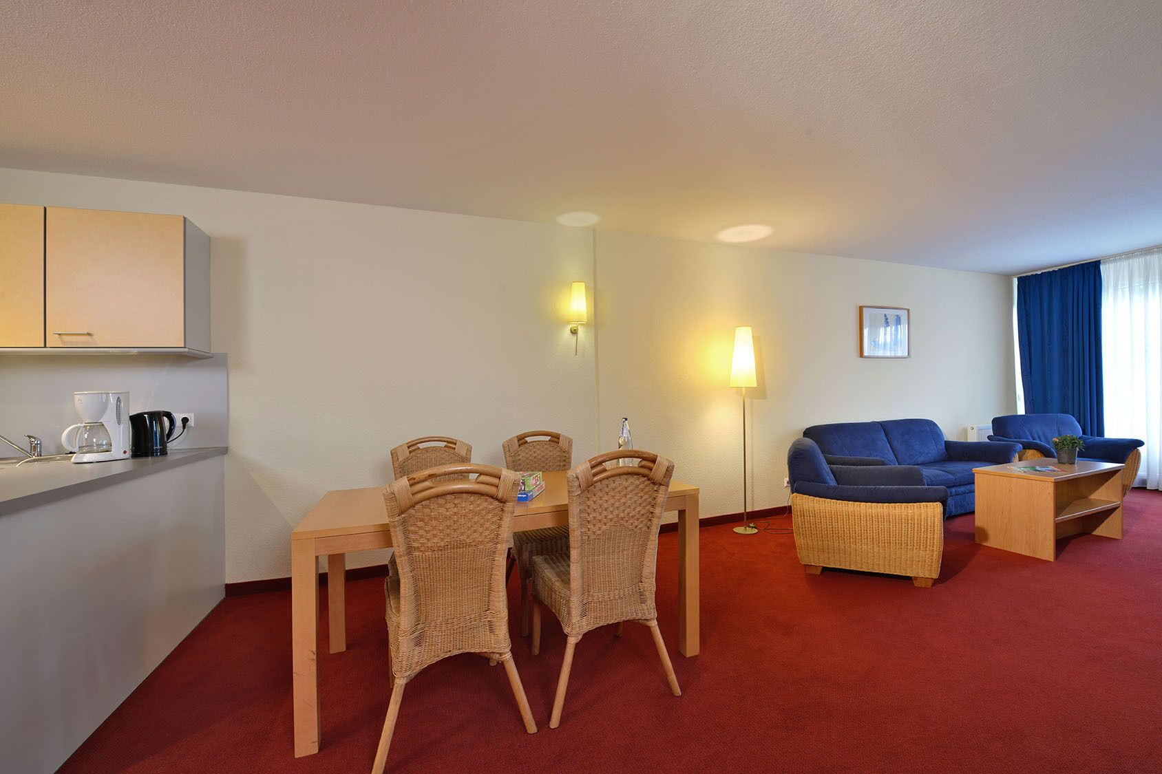 A hotel room with a dining area, a sofa, and a coffee station.