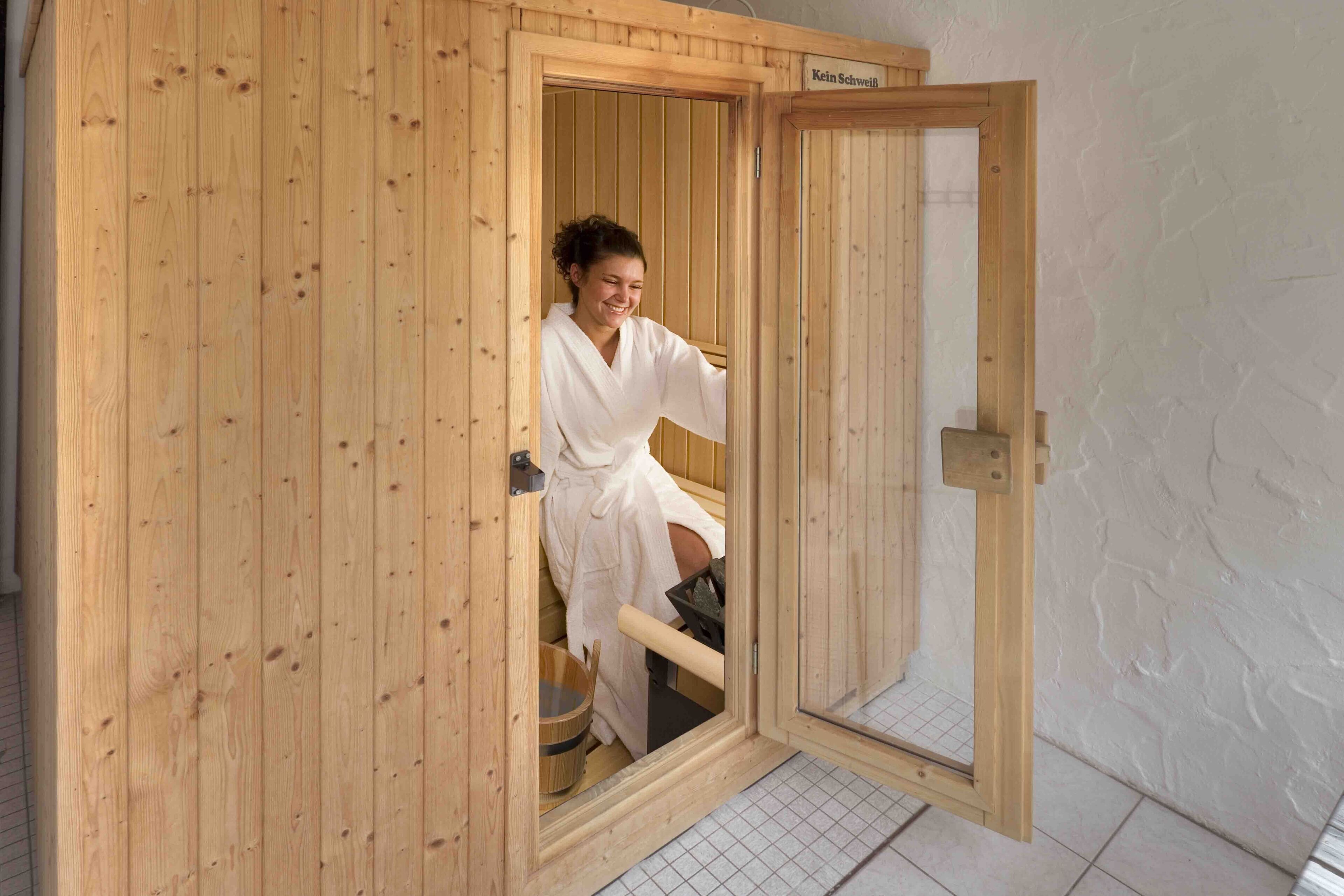 A wooden sauna with a sliding door, a wooden bench inside, and a small wooden bucket.