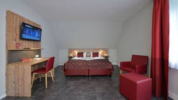 Una habitación de hotel con una cama, un escritorio, una silla y un televisor fijado a un panel de madera.