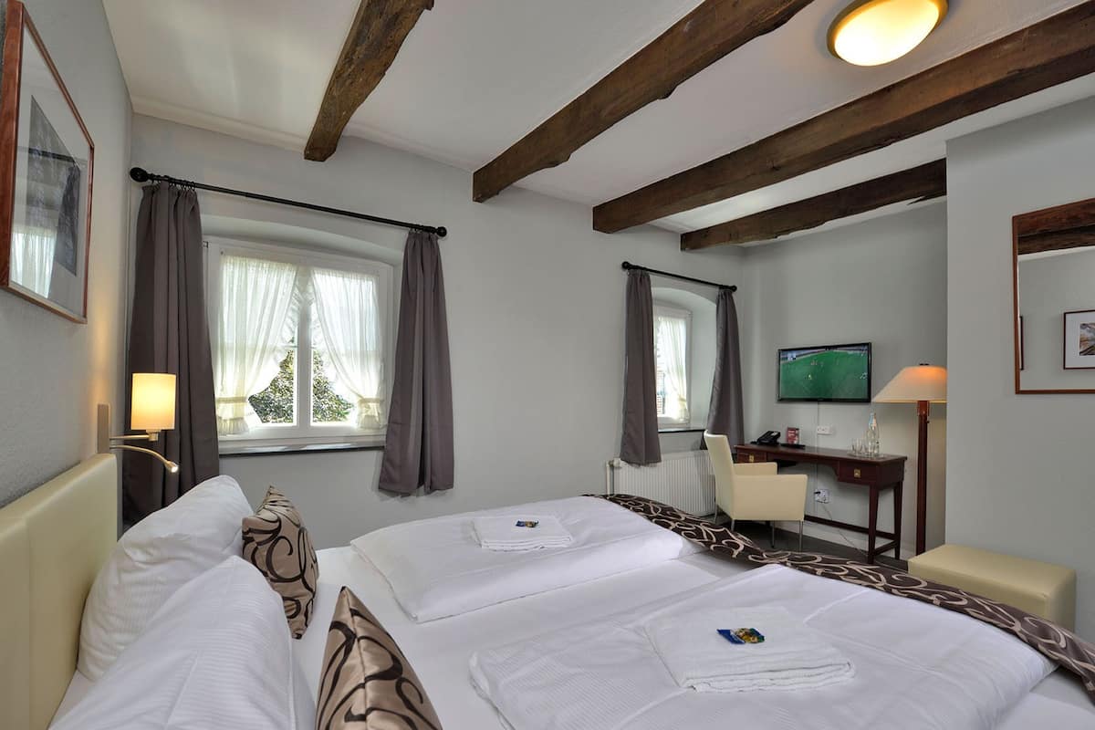 A hotel room with two beds, a desk, a chair, a TV, and a window with curtains.