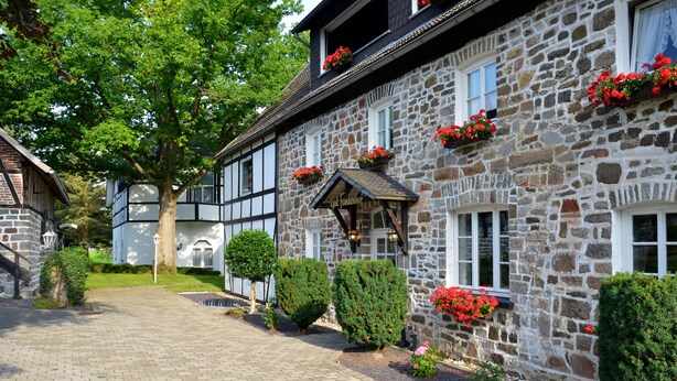 A stone building with a traditional facade, a paved walkway, and neatly trimmed hedges. - Gut Funkenhof (Sundern)