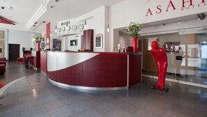 A reception area with a curved counter, a red statue, and a clock. - Hotel Asahi (Düsseldorf)