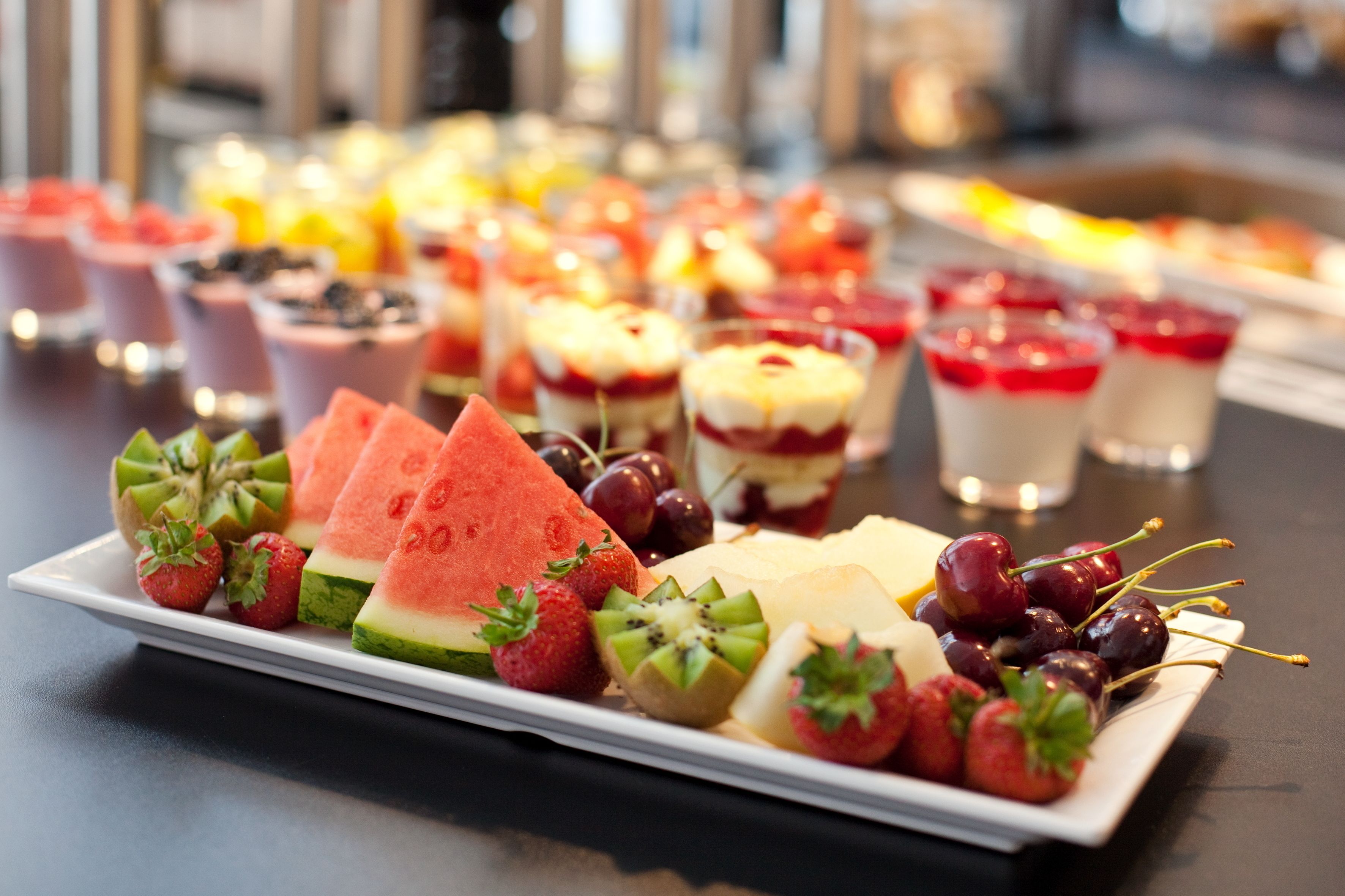 A variety of desserts and fruits on a white plate, including watermelon, strawberries, kiwi, and cherries.