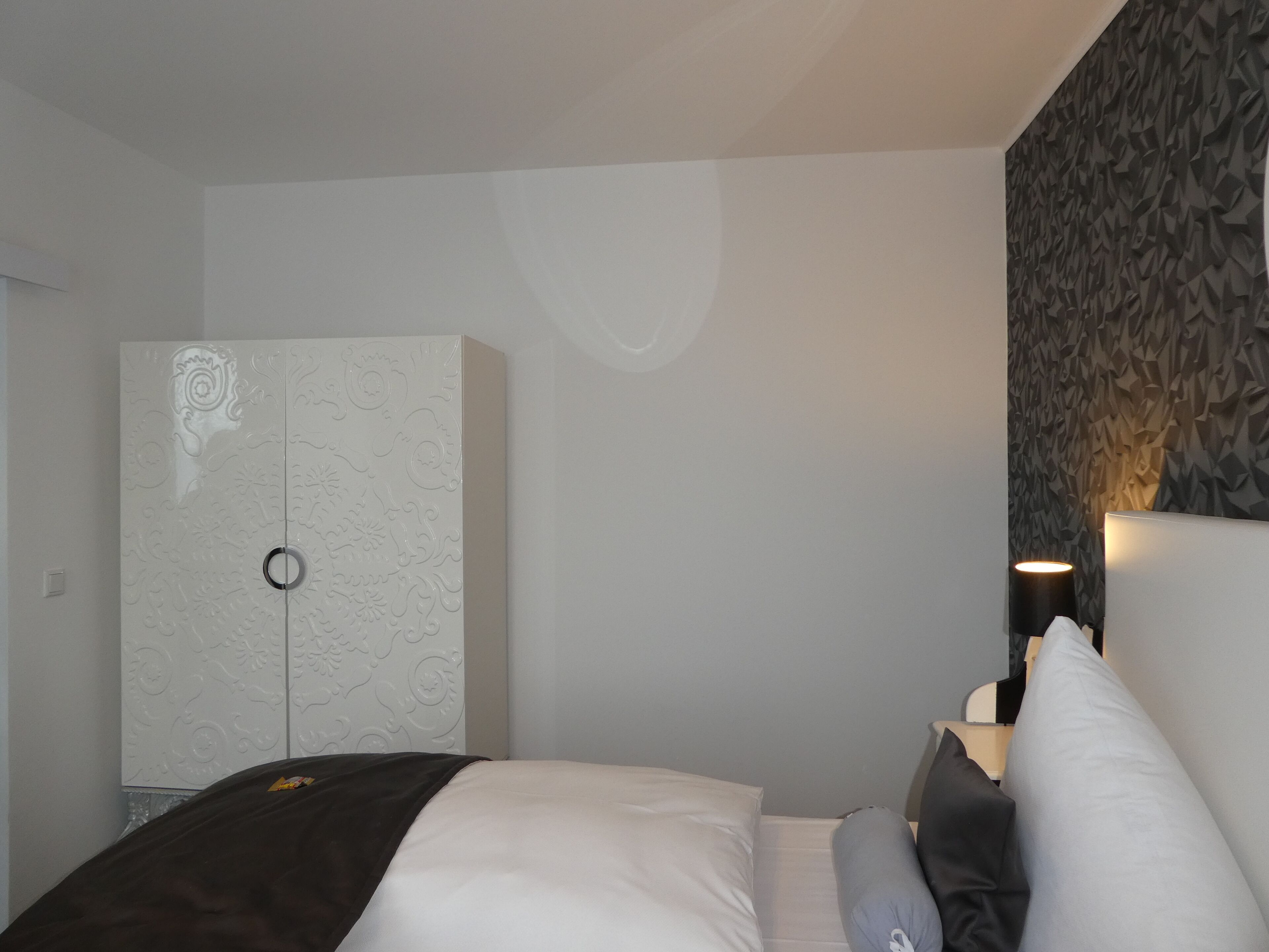 Een slaapkamer met een bed, een kledingkast en een muur met een geometrisch patroon.