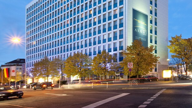 A modern hotel building with a grid of windows, a prominent sign reading "Hotel Asahi," and a website address displayed on the facade. - Hotel Asahi (Düsseldorf)