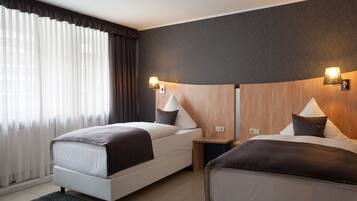 Una habitación de hotel con dos camas, un ventanal con cortinas translúcidas y lámparas fijadas a la pared.