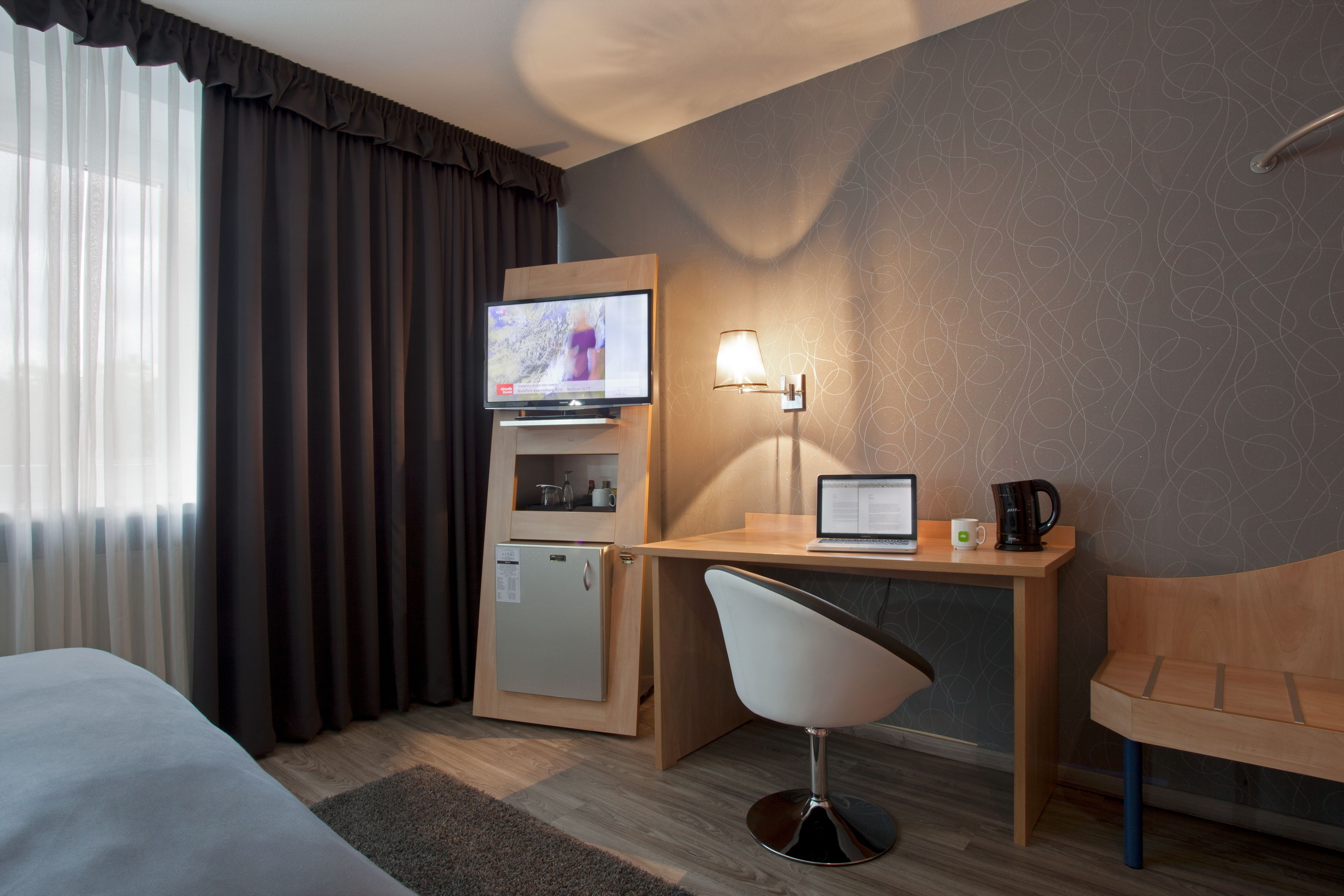 Habitación de hotel con cama, escritorio, computadora portátil, televisor, refrigerador y una silla.