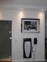 Una parete con una fotografia in bianco e nero incorniciata, un'opera d'arte geometrica e una porta con un pannello di vetro.