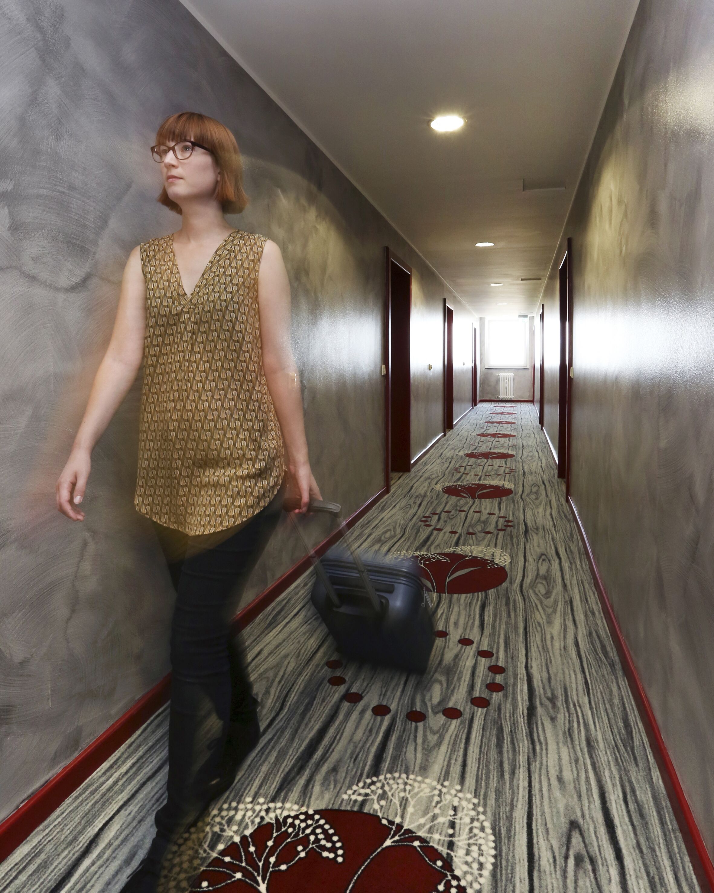 Una persona che cammina lungo un corridoio con tappeto a motivi e porte su entrambi i lati.