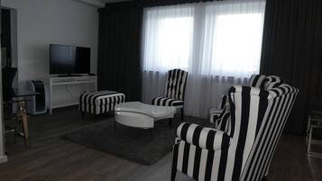 A modern living room with a flat-screen TV, a white coffee table, and striped armchairs.