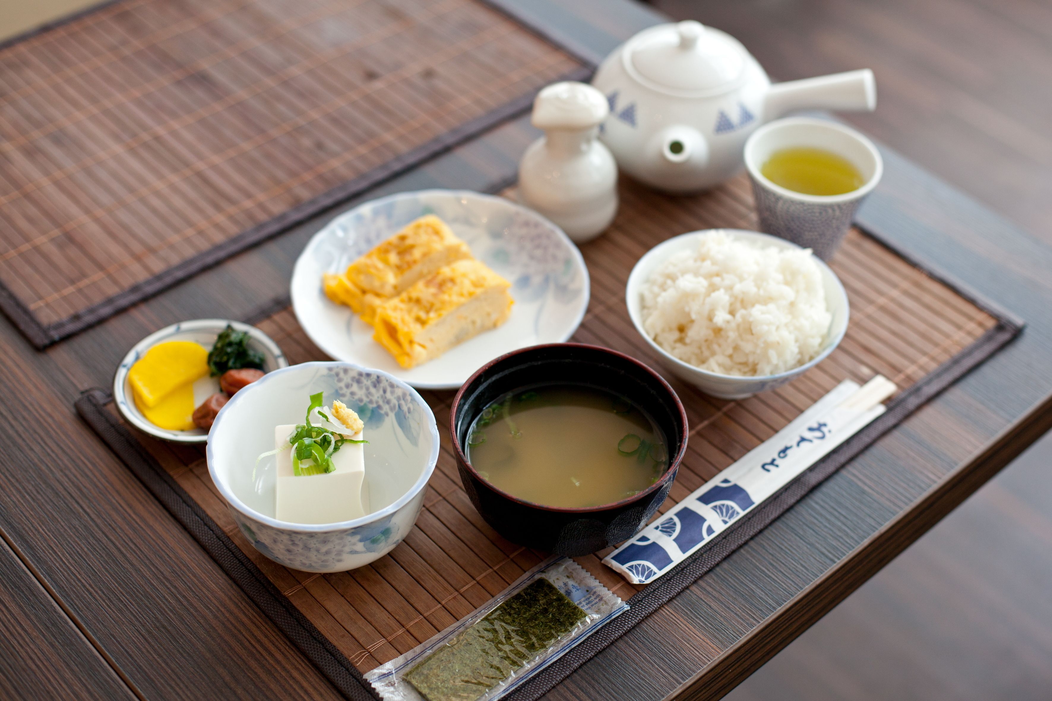Un montaje tradicional de comida japonesa con tetera, arroz, sopa y varios platos sobre una mesa de madera.