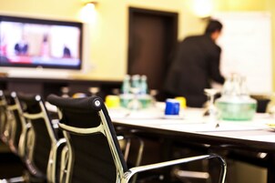 Una sala conferenze con un lungo tavolo, sedie e uno schermo televisivo.