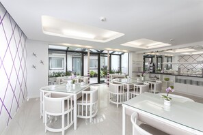 A modern, well-lit dining area with white furniture and glass tables, featuring a view of the outdoors through large windows. - Hotel Prinz Anton (Düsseldorf)
