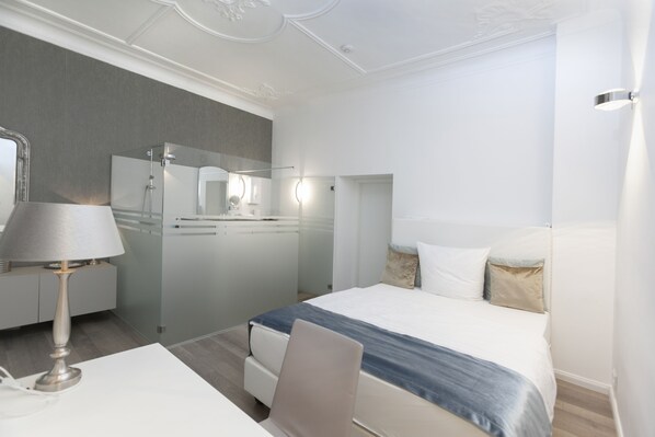 A modern hotel room with a bed, bedside table, lamp, and a bathroom with a shower and mirror. - Hotel Prinz Anton (Düsseldorf)