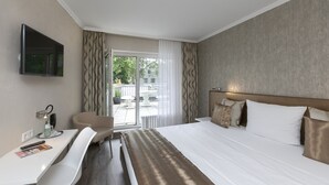 Ett hotellrum med en säng, ett skrivbord, en stol, en tv och utsikt över omgivningarna.