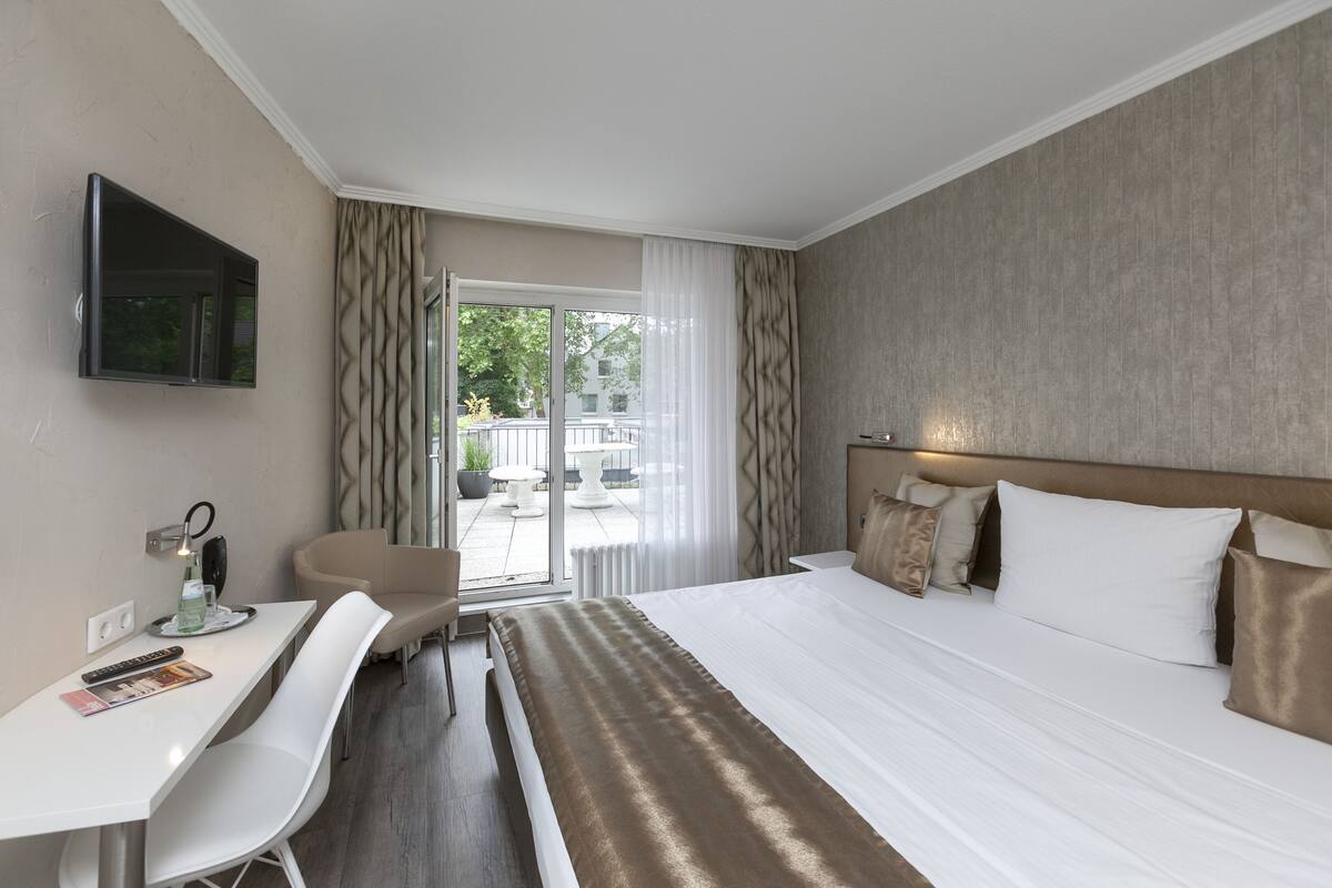 Una habitación de hotel con cama, escritorio, silla, televisor y vistas al exterior.