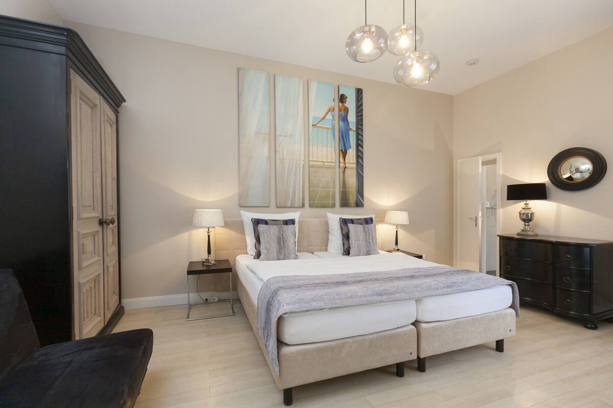 Un dormitorio con una cama grande, mesitas de noche con lámparas, un armario y un cuadro en la pared.
