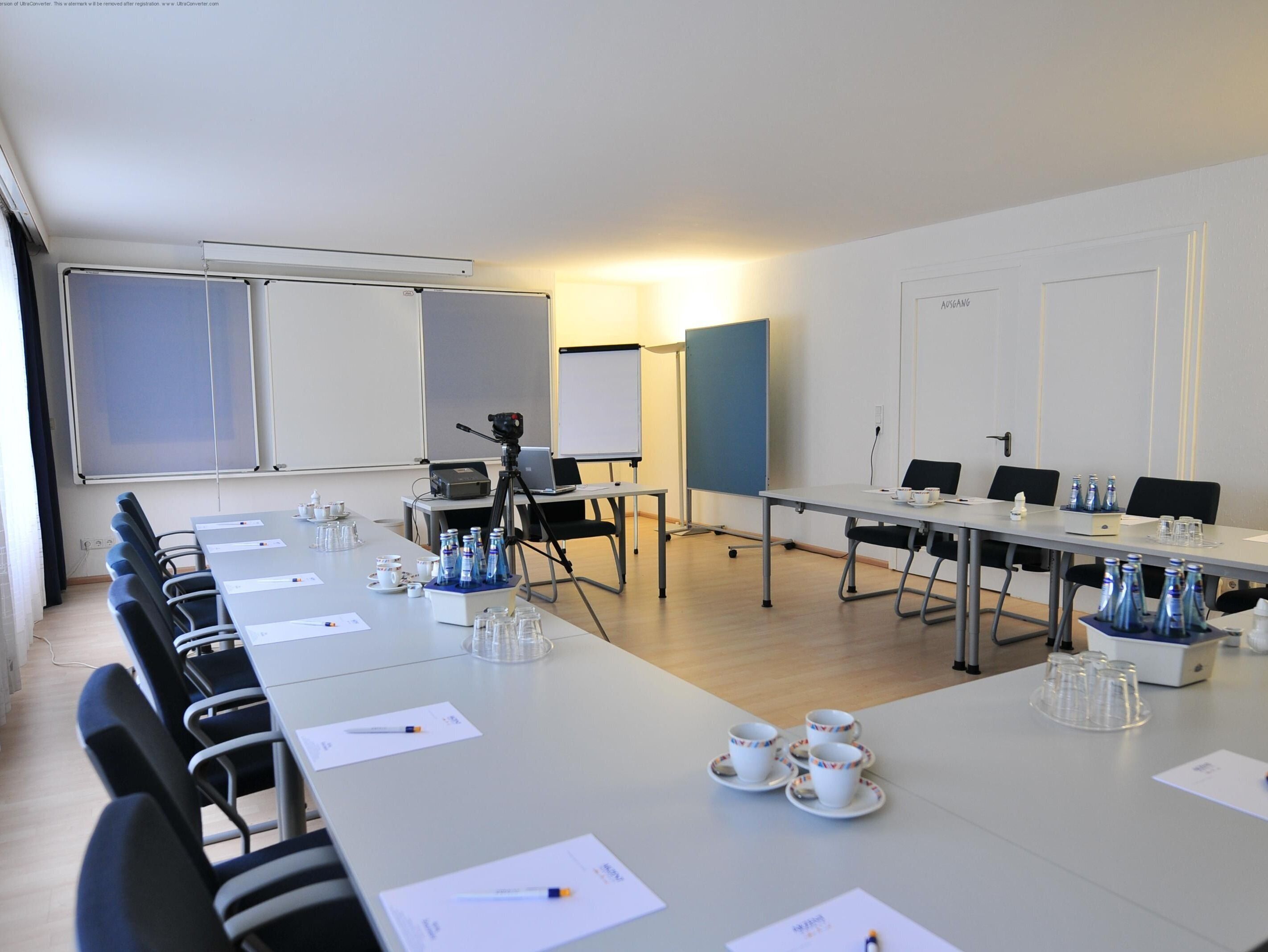 Ein Konferenzraum mit einem langen Tisch, Stühlen, einem Stativ und Präsentationsbildschirmen.