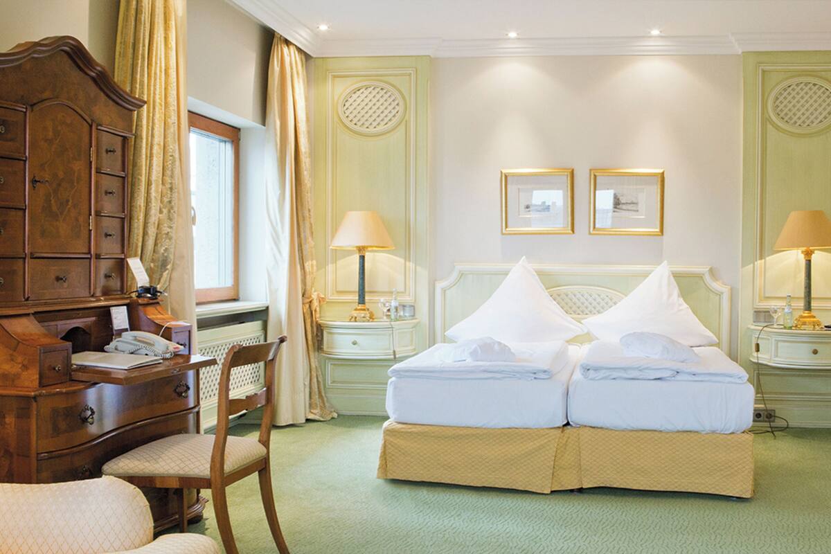 A hotel room with a bed, a desk with a telephone, a chair, and two bedside tables with lamps.
