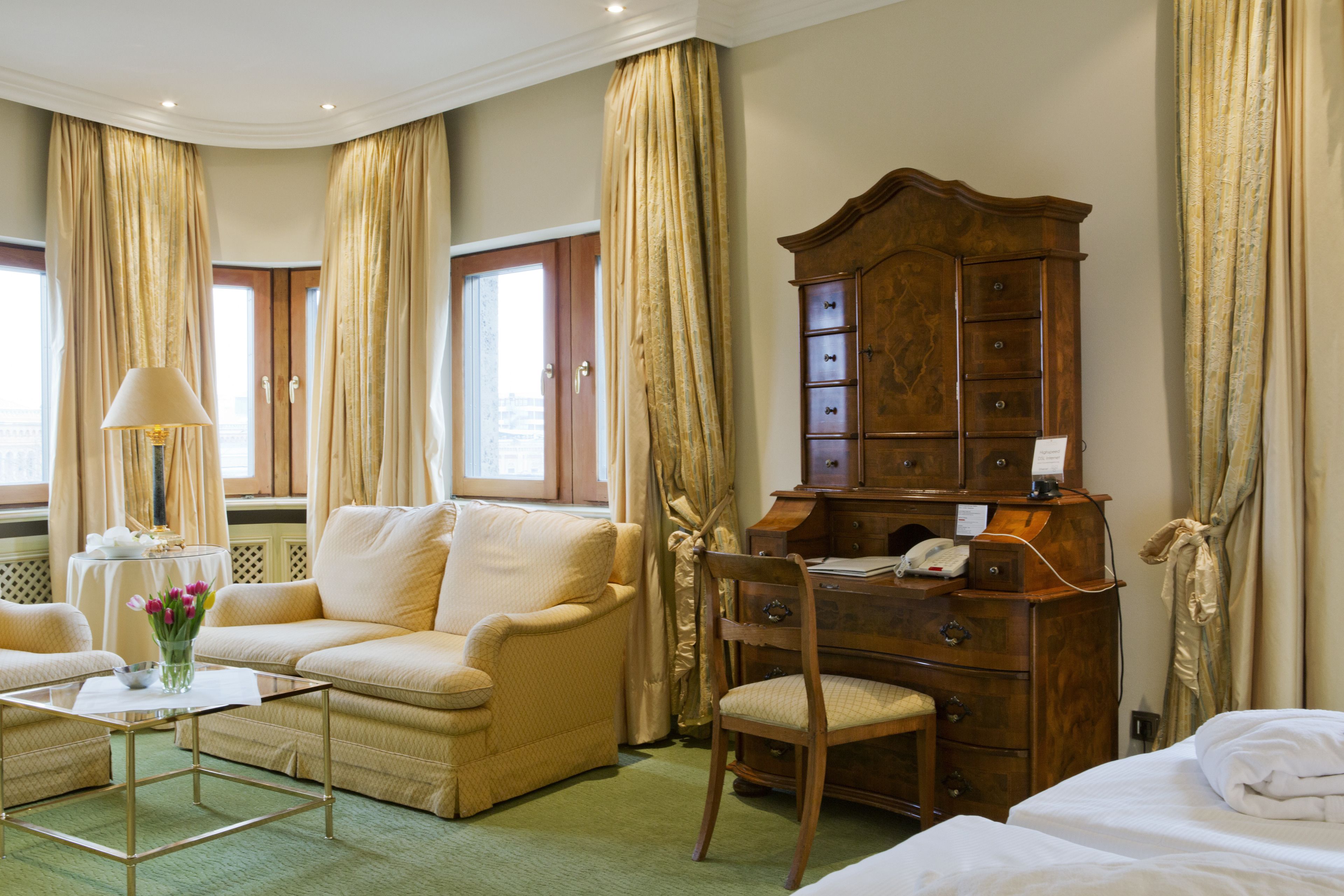 A hotel room with a sofa, a wooden dresser, a chair, a small table with a lamp, and a bed.