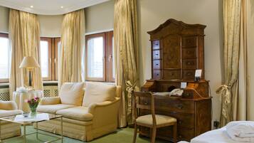 A hotel room with a sofa, a wooden dresser, a chair, a small table with a lamp, and a bed.