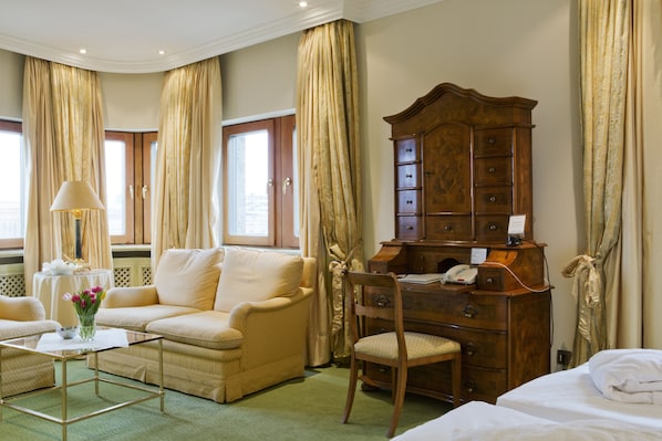 A hotel room with a sofa, a wooden dresser, a chair, a small table with a lamp, and a bed.