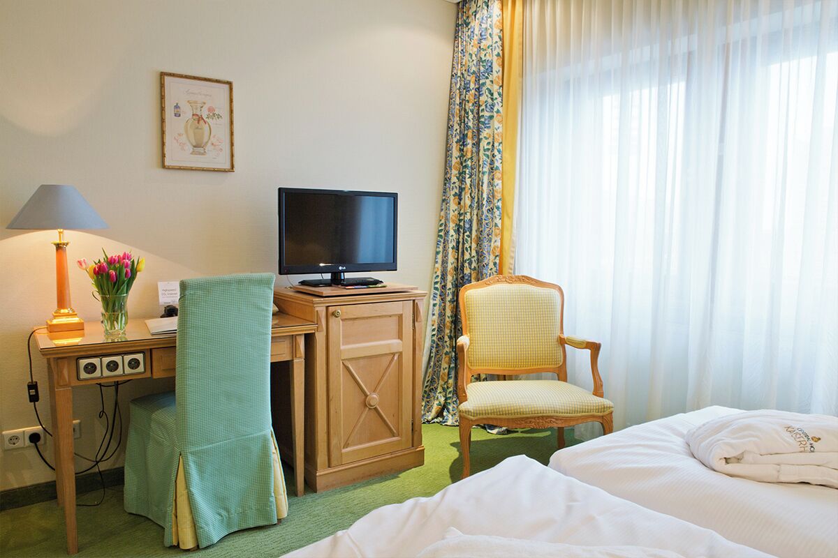 Una habitación de hotel con una cama, un escritorio con una computadora, una lámpara y una silla.