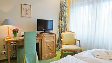 Una habitación de hotel con una cama, un escritorio con una computadora, una lámpara y una silla.