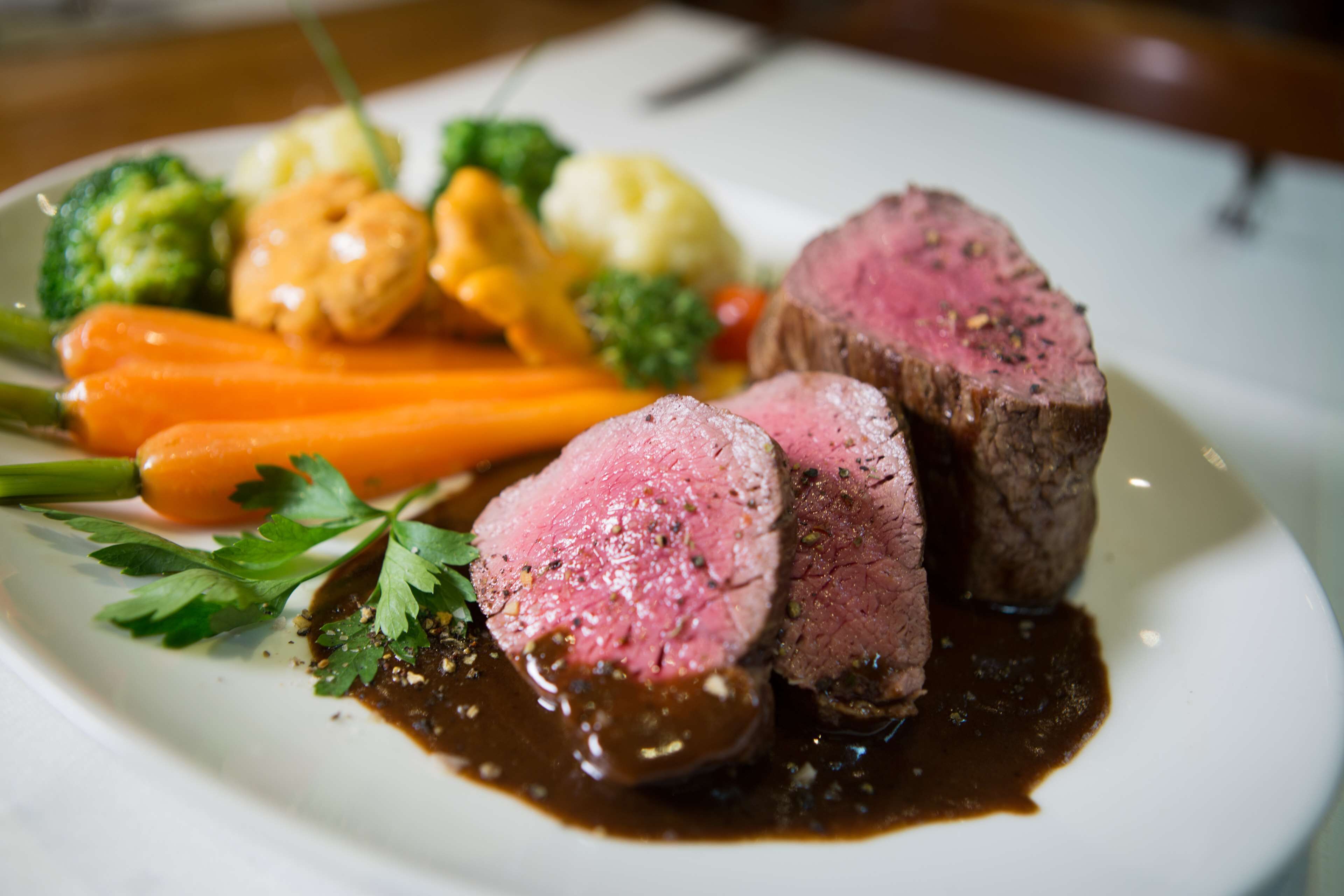 Ein Teller Essen mit Steak, Karotten, Brokkoli und Blumenkohl.