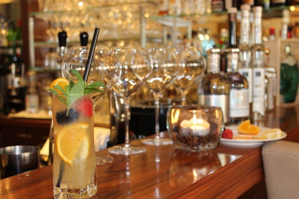 A bar setting with a tall glass containing a beverage garnished with a lemon slice and mint leaves, a candle, and a plate with fruit.