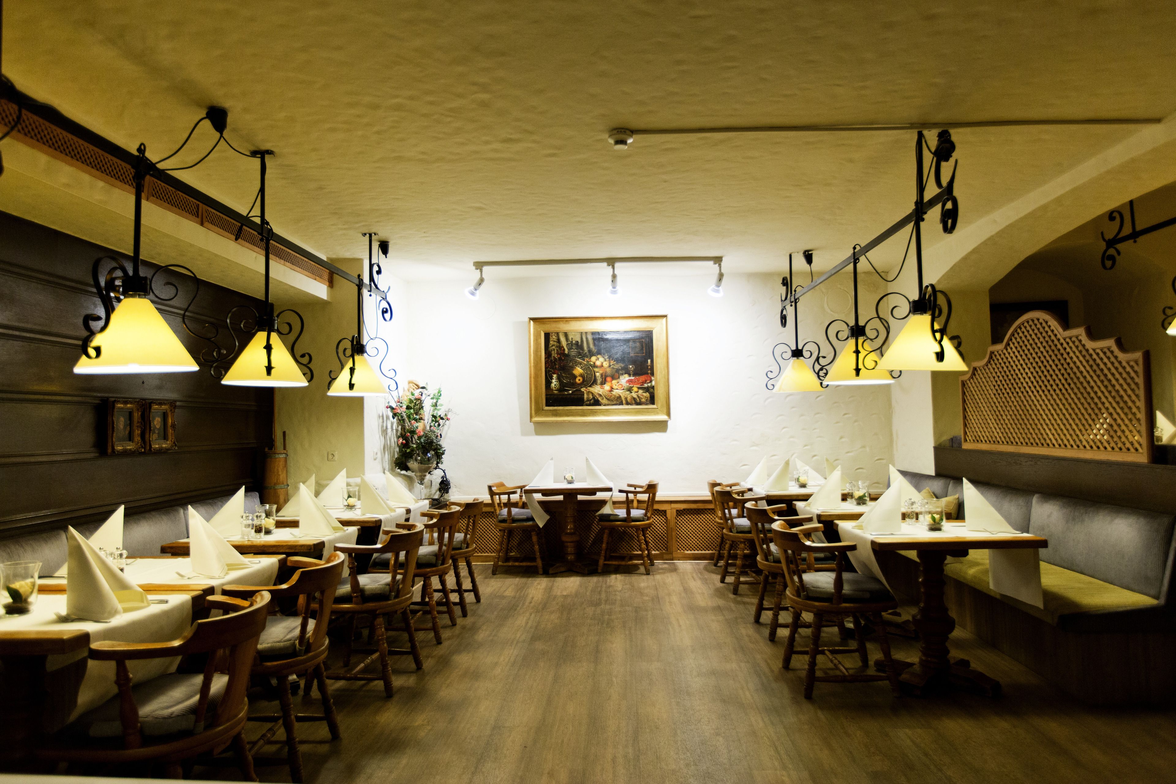 A restaurant with wooden tables and chairs, hanging pendant lights, and a framed painting on the wall.