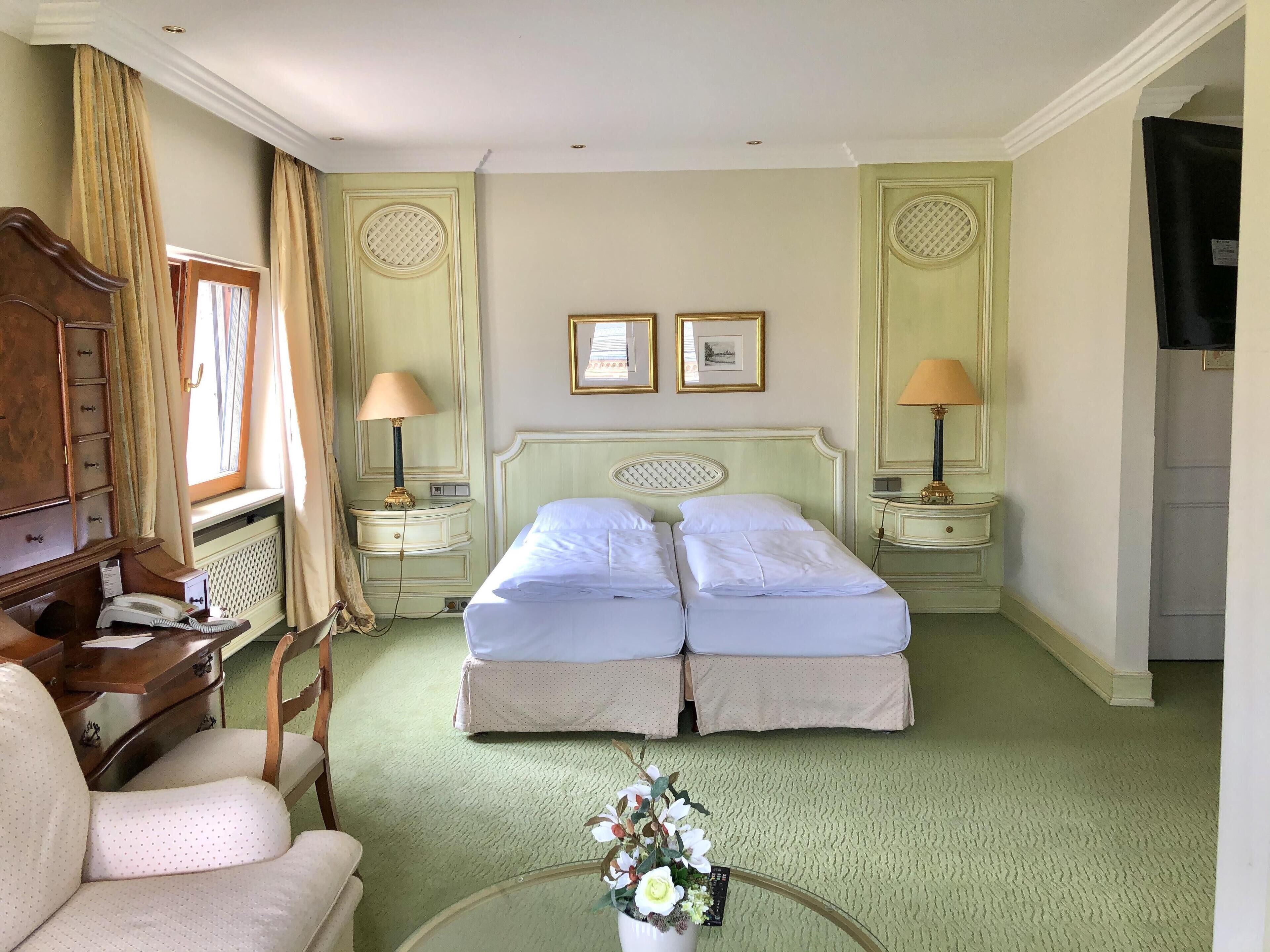 A hotel room with two beds, a desk, a chair, a TV, and a window with curtains.