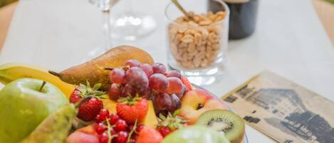 Una mesa con una bandeja de frutas, una botella de vino, una copa de vino y un cuenco pequeño de nueces.