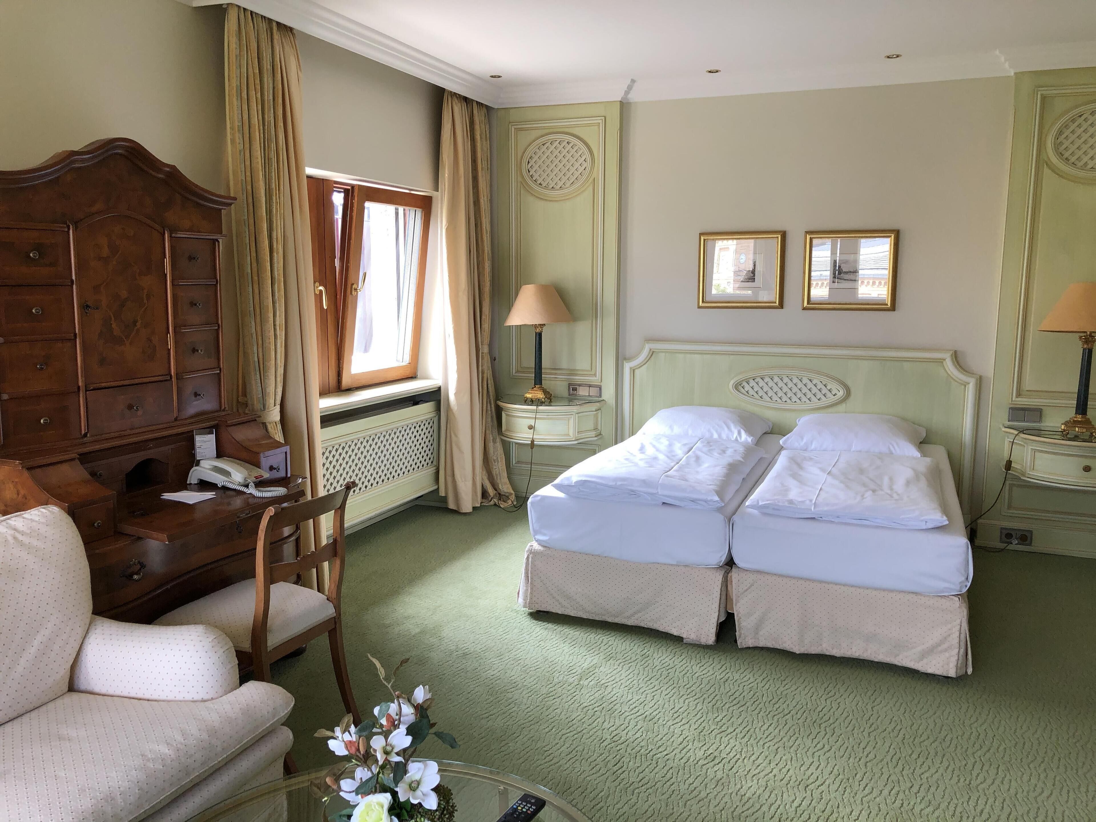 Habitación de hotel con cama, escritorio, silla, lámpara y ventana con cortinas.