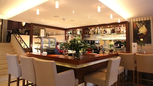 A bar area with a wooden counter, bar stools, and a variety of bottles and glasses. - Central-Hotel Kaiserhof (Hannover)