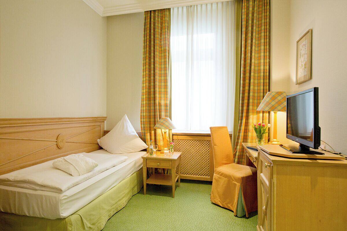 A hotel room with a bed, a desk, a television, and a window with curtains.