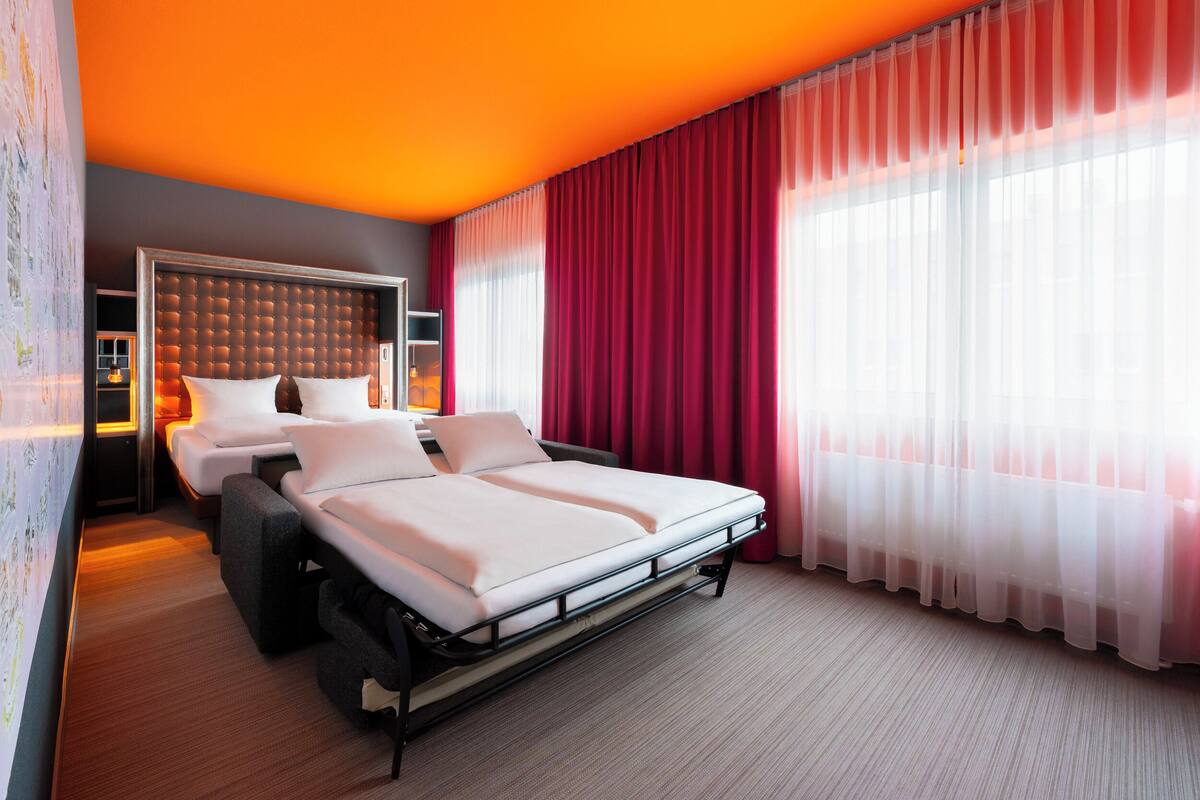 Een hotelkamer met een bed, een zithoek en een groot raam met gordijnen.