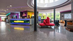 A modern lobby with a central reception desk, a red seating area, and a large window providing a view of the outdoors. - Designhotel Wienecke XI. Hannover (Hannover)